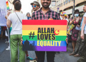 Just Me and Allah: A Queer Muslim Photo Project A photograph of a Muslim man holding a rainbow colored sign that reads, "Allah Loves Equality."