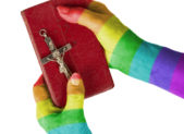 Gay Christians: An Oxymoron? A photo of a woman with rainbow-painted hands holding a Bible and a crucifix.