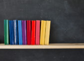 LGBT Novels with Happy Endings Rainbow-colored books stacked alongside one another.