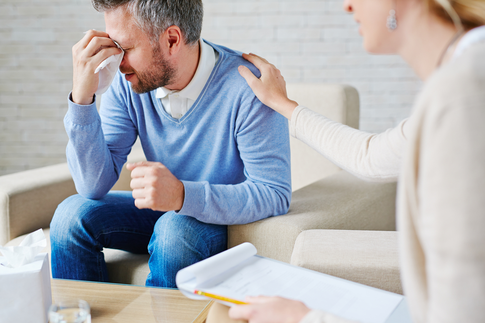 A man crying. A female psychiatrist has her hand on his shoulder.