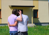 A History of Housing Discrimination Against Homosexual Couples A homosexual couple embrace one another in front of their home.