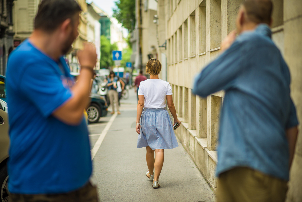 Two men catcall a woman walking down the street.