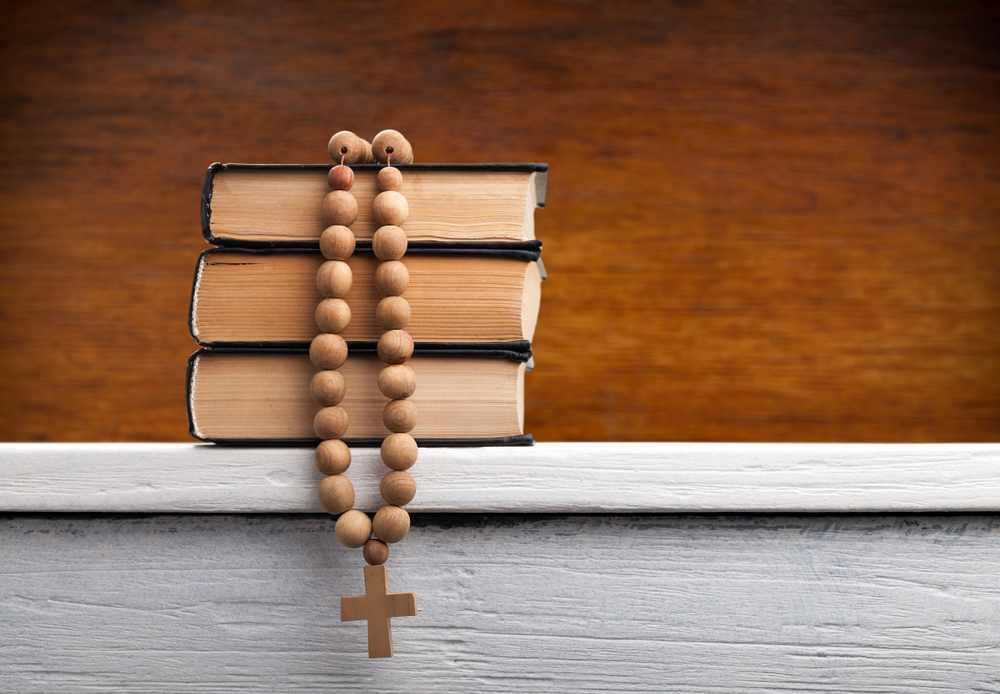 A stack of books with a rosary laid on top.