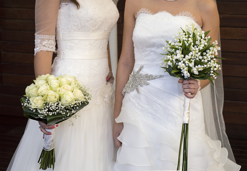 Two women in white wedding gowns holding bouquets.