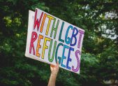 Activist Group Reunites Gay Refugee Couple An activist holds a sign that reads, "With LGBT refugees."
