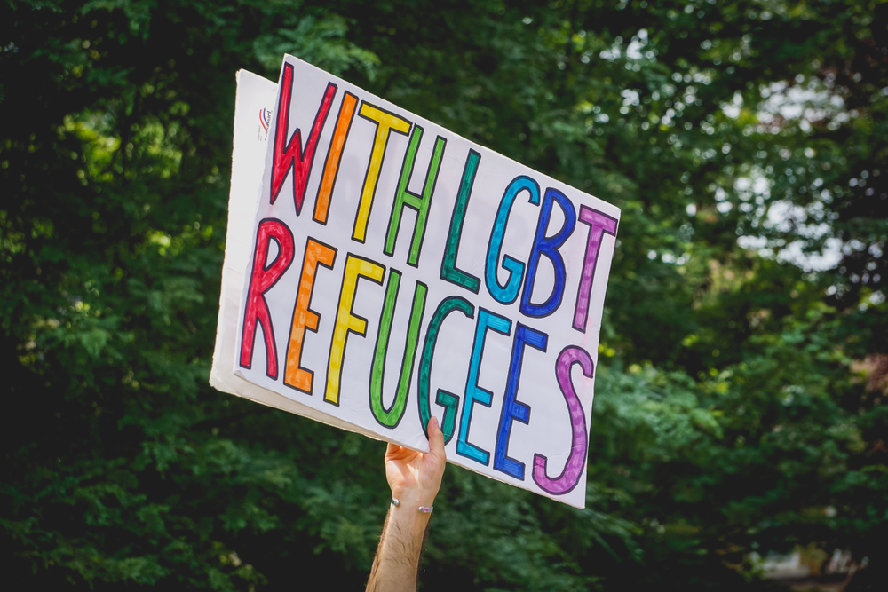 An activist holds a sign that reads, "With LGBT refugees."