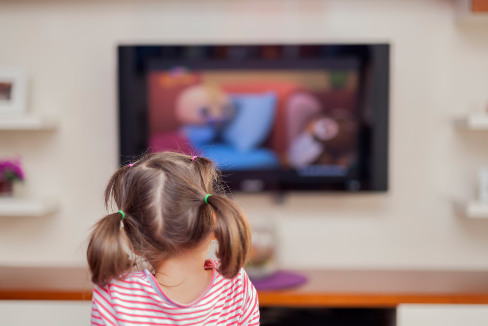A photo of a young girl in pigtails watching a TV show.