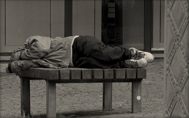 A homeless person sleeping on a bench.