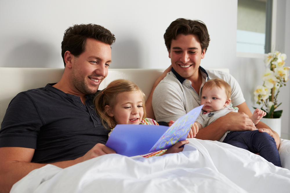 Two gay dads read to their two children in bed.