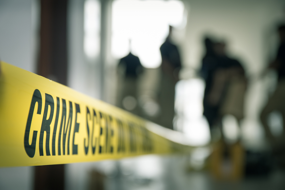A photo of crime scene tape with blurred figures in the background.