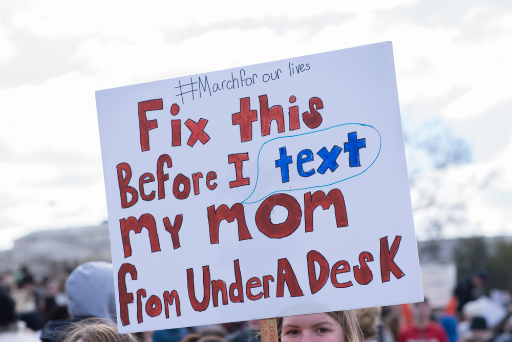A National School Walkout demonstrator holds a sign that reads, "Fix this before I text my mom from under a desk."