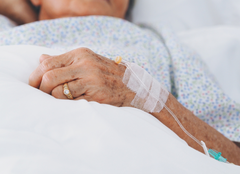 A sick elderly woman in a hospital bed. She is wearing a wedding band.